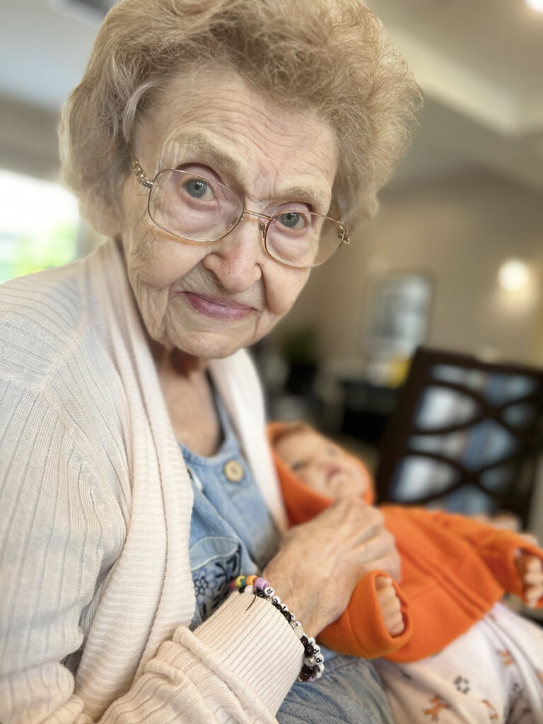 An older woman, Margie, cradles a baby doll with a tender smile.