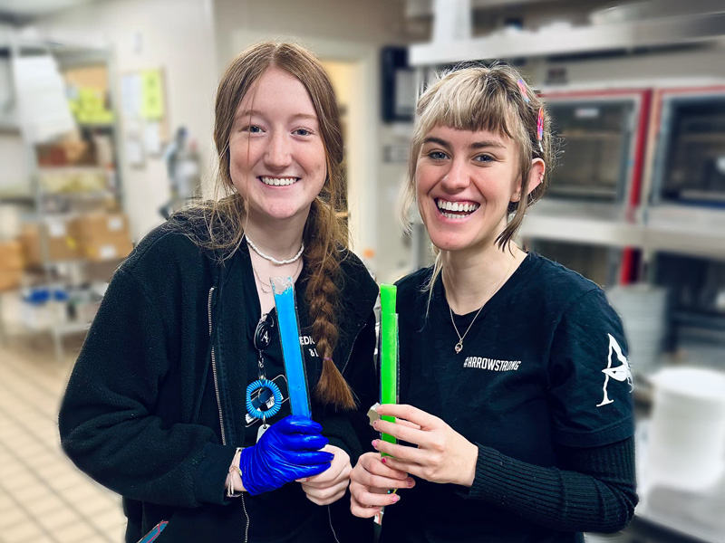 Two employees at The Westbury Senior Living smile while holding colorful frozen treats, celebrating National Chili Day with a chilly surprise.