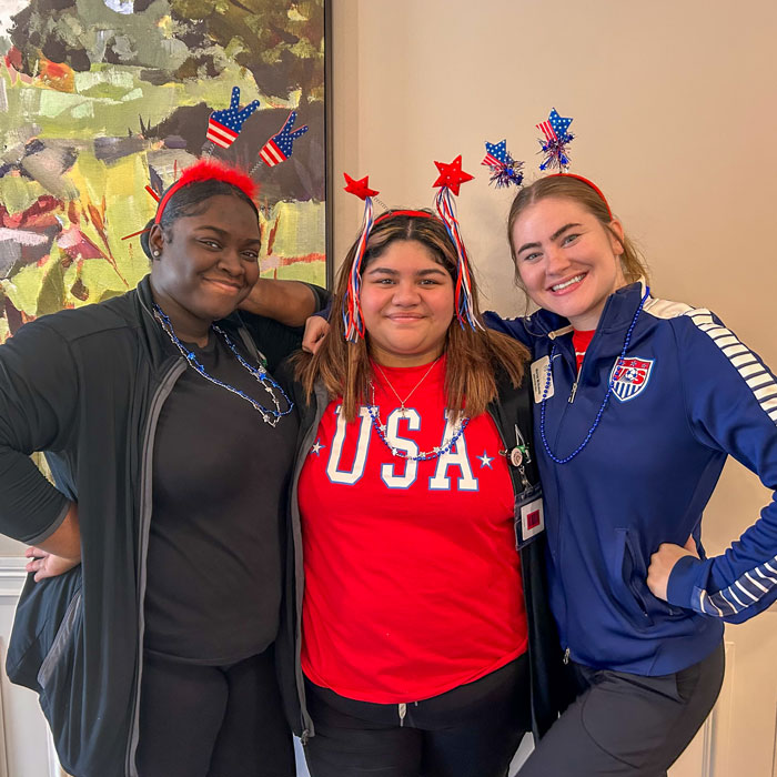 Three team members wearing festive USA-themed outfits and accessories, celebrating together with smiles during a patriotic event at Vitalia North Olmsted Senior Living community.