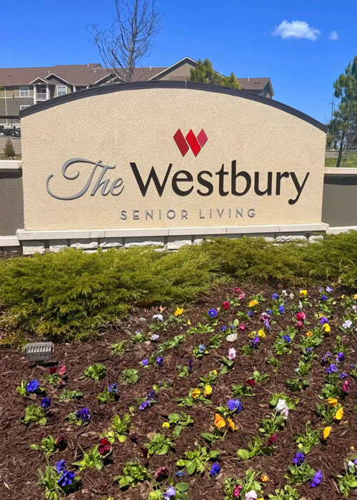 Front sign for The Westbury Senior Living stands behind a freshly mulched flower bed filled with colorful spring blooms.