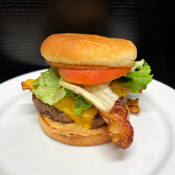 Cheeseburger with bacon, lettuce, tomato, and a layer of peanut butter on a toasted bun, combining bold, sweet, salty, and savory flavors in one bite.