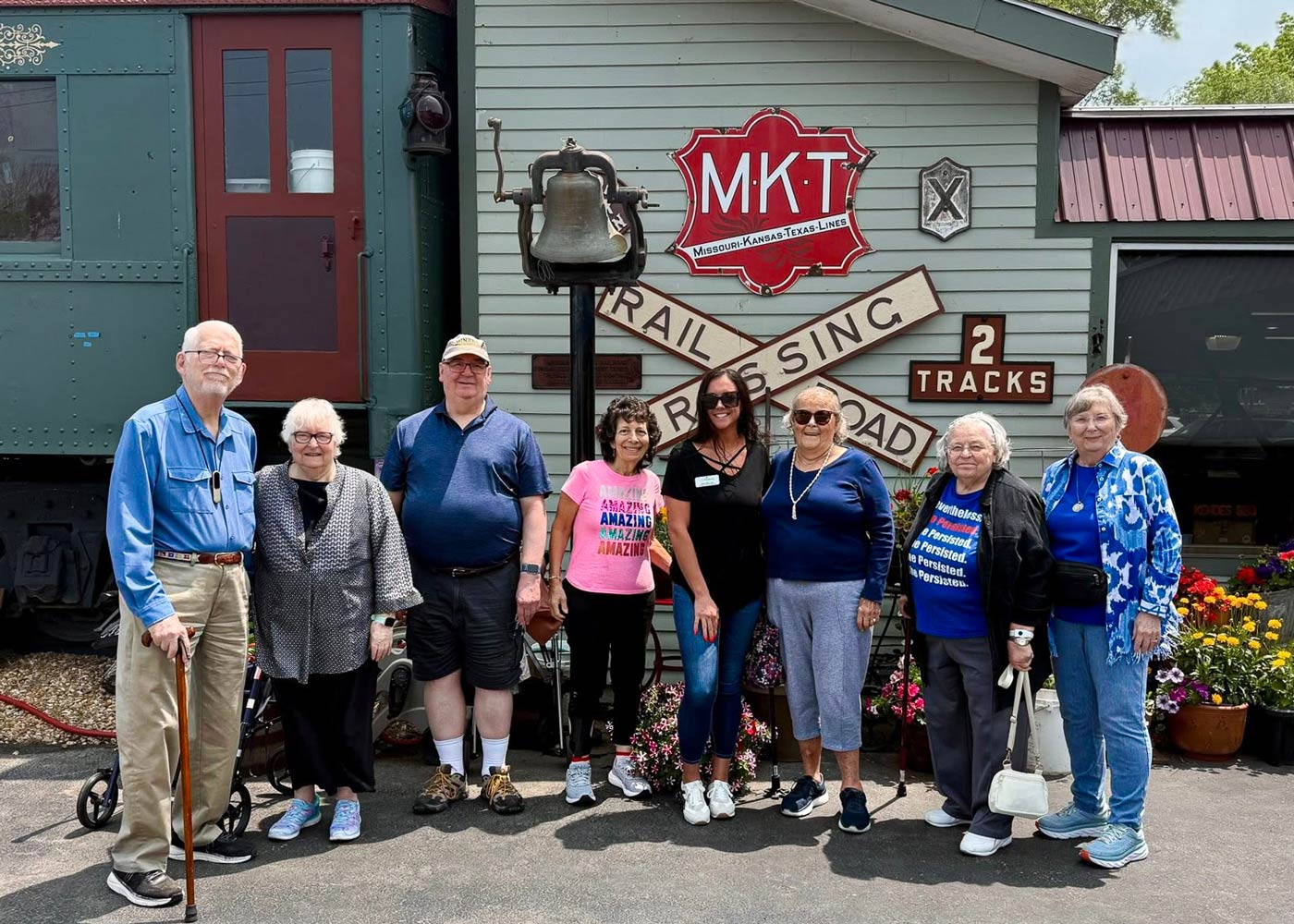 Group of seniors and staff smiling together in front of the historic MKT railroad car and sign during an outing