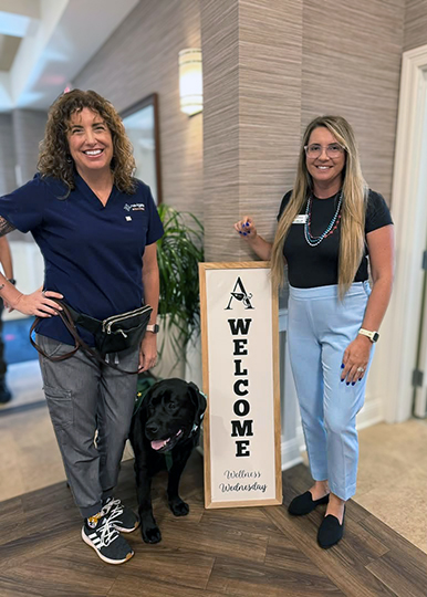 Two team members smile next to a Welcome sign at The Westbury Senior Living.