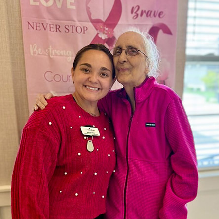 A team member and senior woman smile together during a Breast Cancer Awareness event.