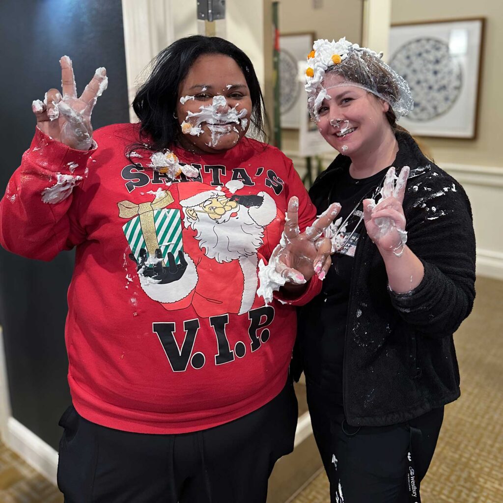 Two team members at The Westbury smile and flash playful peace signs, covered in pie and whipped cream after a fun event.