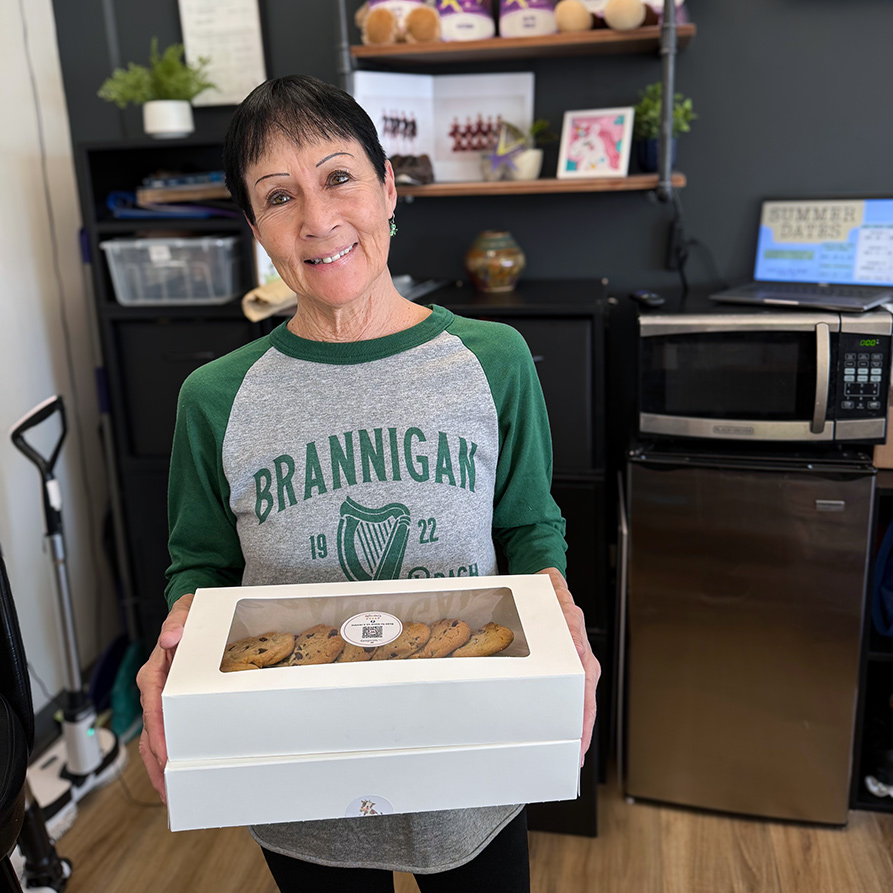 A woman smiles at a local business, holding two boxes of delicious cookies.
