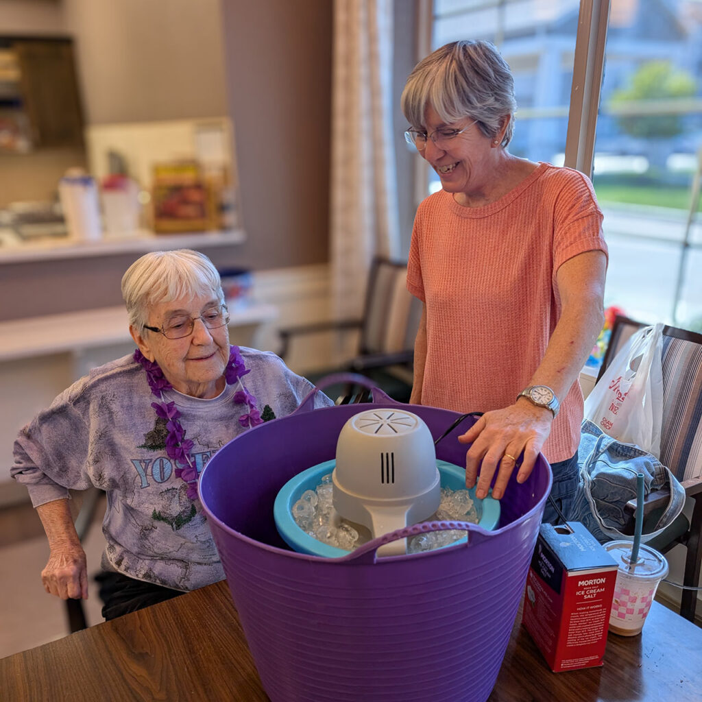 Two women smile while making homemade ice cream at The Westbury Senior Living.