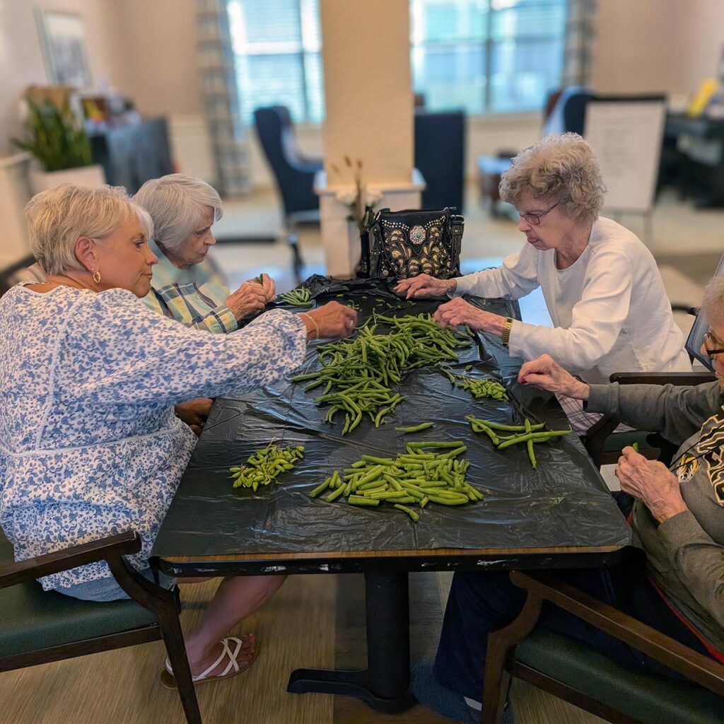 Four senior women prepare fresh green beans at The Westbury Senior Living.